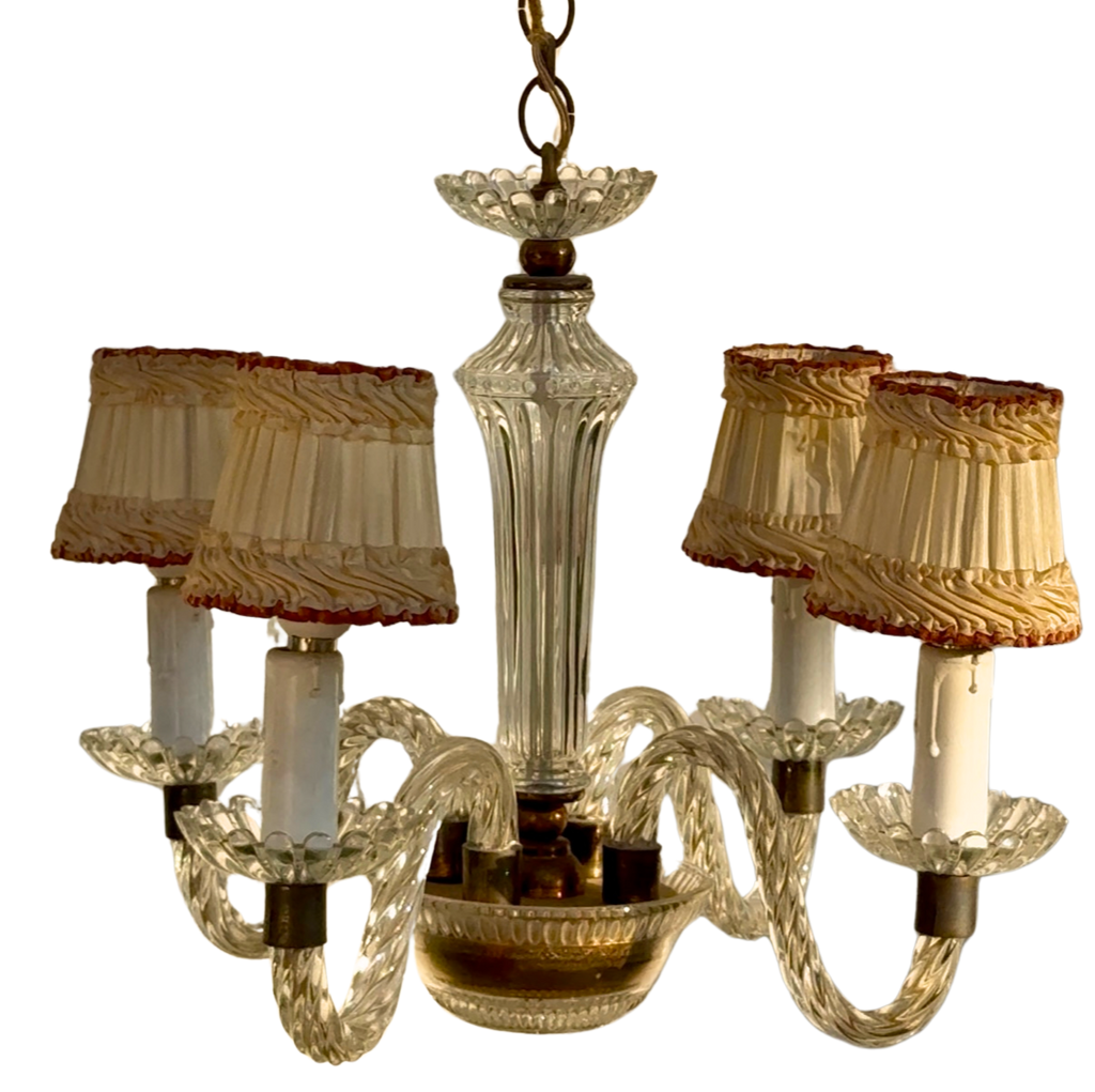 A vintage five-light chandelier featuring a clear ribbed glass central column and twisted glass arms, with cream pleated fabric shades trimmed in red and gold, set against a plain white background.