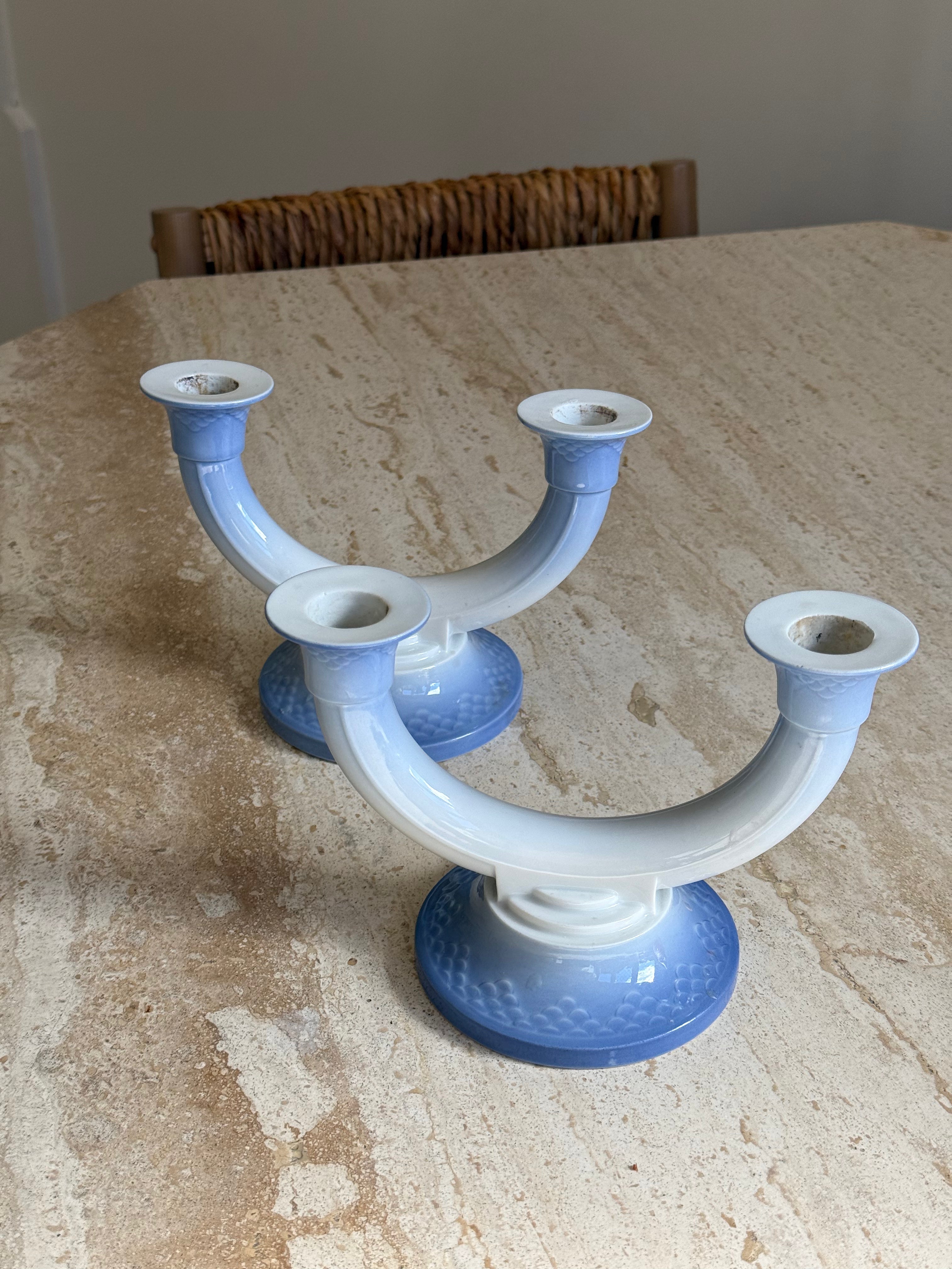 A pair of U-shaped ceramic candlesticks with white bodies and blue bases, displayed on a beige stone tabletop.