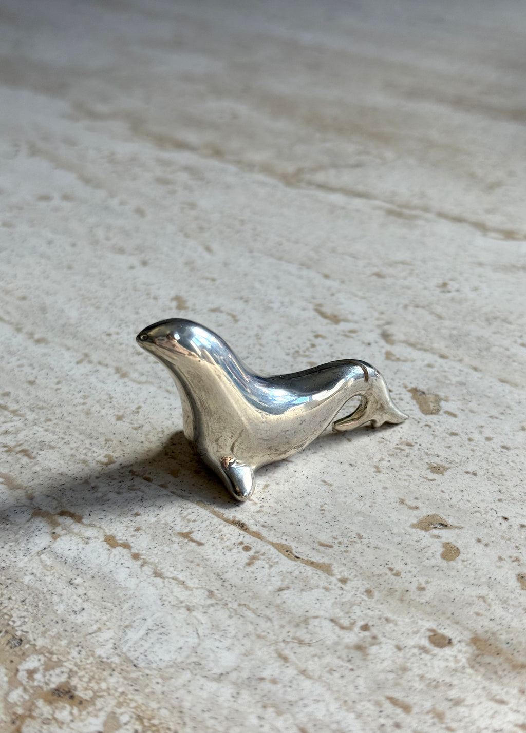 A small polished silver seal figurine resting on a textured beige stone surface.