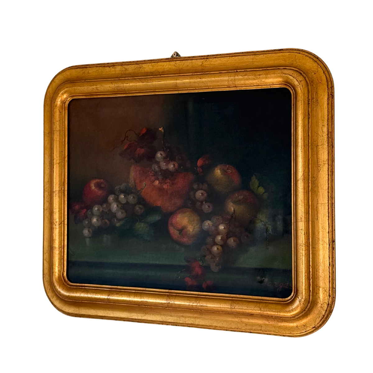 A framed still life oil painting depicting a cluster of red apples, purple grapes, and a pomegranate on a dark background, housed in a wide, ornate gilded gold frame.