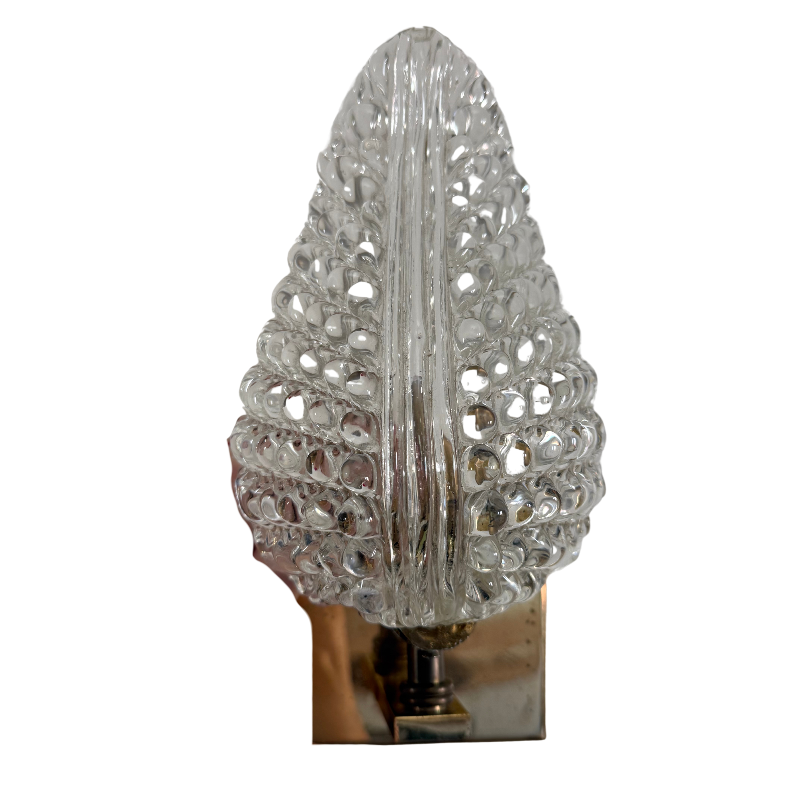 A decorative clear glass wall sconce with an intricate, openwork leaf or tree-like silhouette mounted on a polished metallic base.
