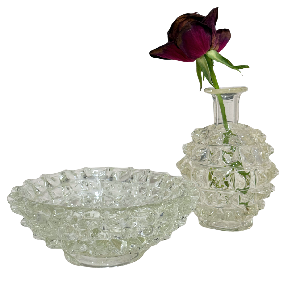 A clear textured glass bowl and matching small glass vase with a dark burgundy rose stem, photographed on a plain white background.