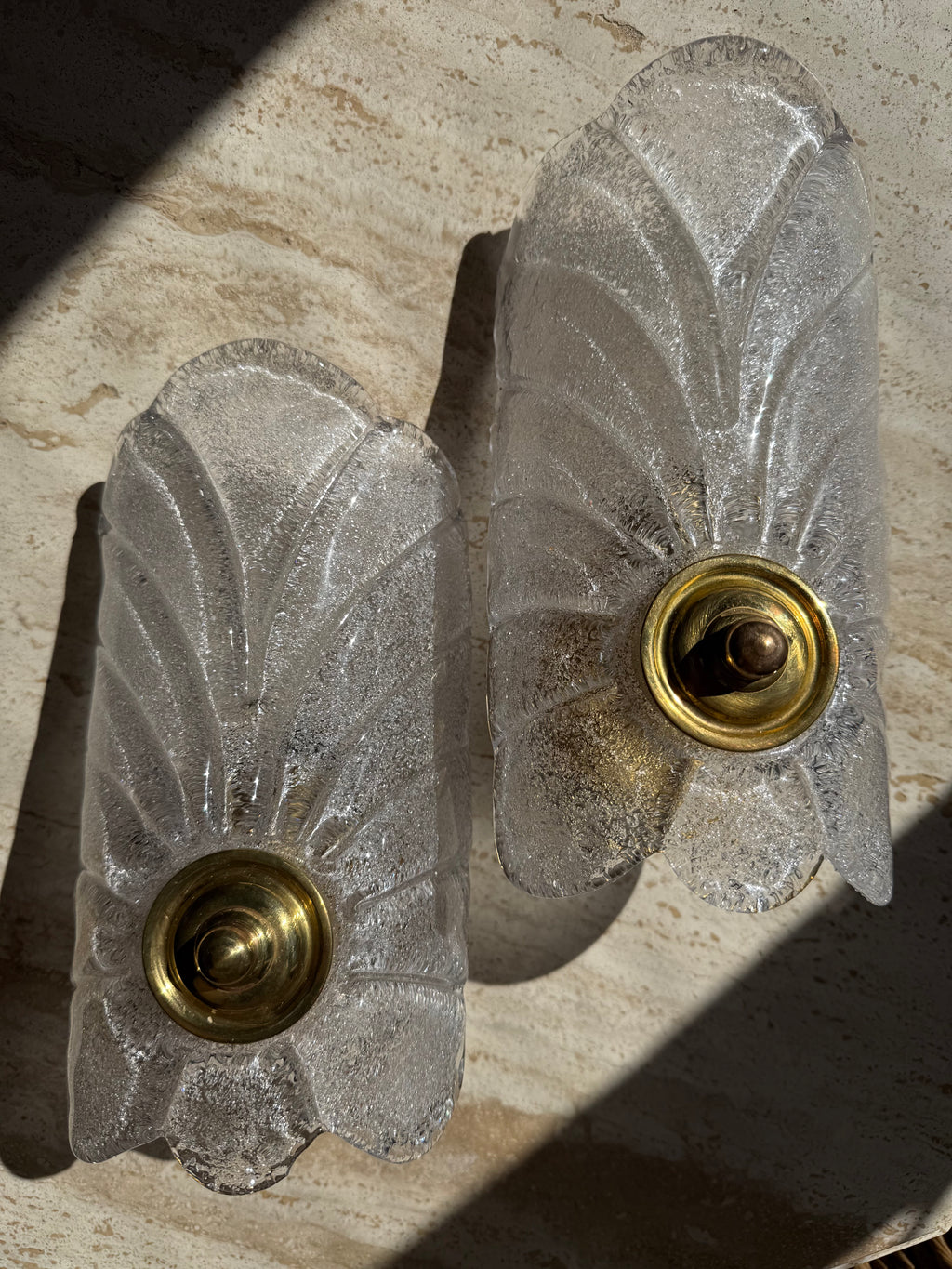 A pair of vintage Art Deco wall sconces made of textured, frosted clear glass with gold brass bases, resting on a beige stone surface.