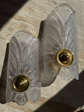 A pair of vintage Art Deco wall sconces made of textured, frosted clear glass with gold brass bases, resting on a beige stone surface.