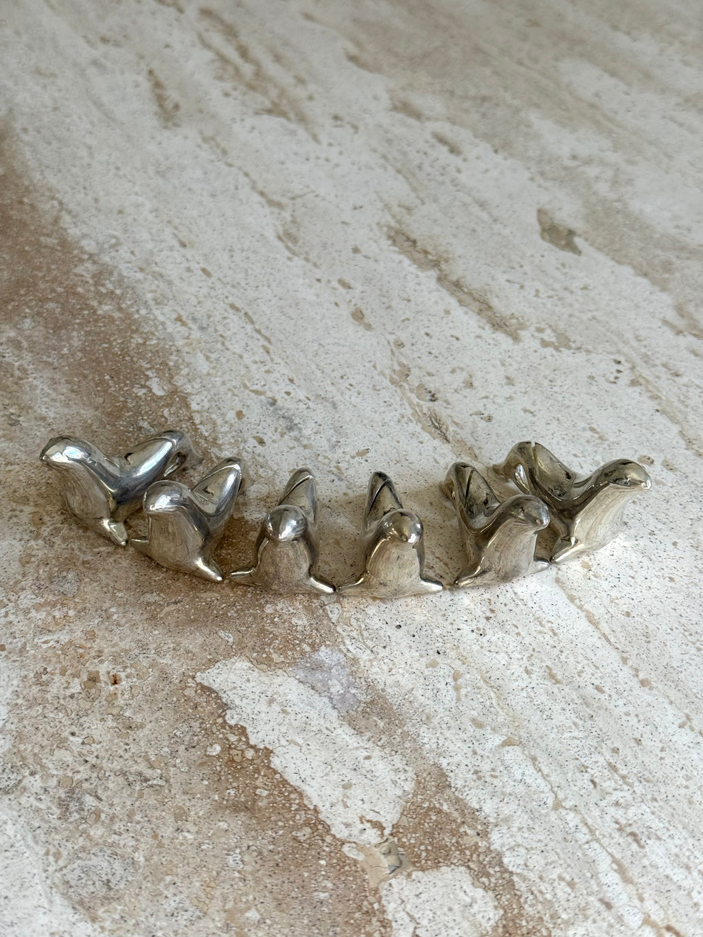 A curved silver-toned metal ring featuring a series of small, stylized bird figures, photographed on a textured beige stone surface.