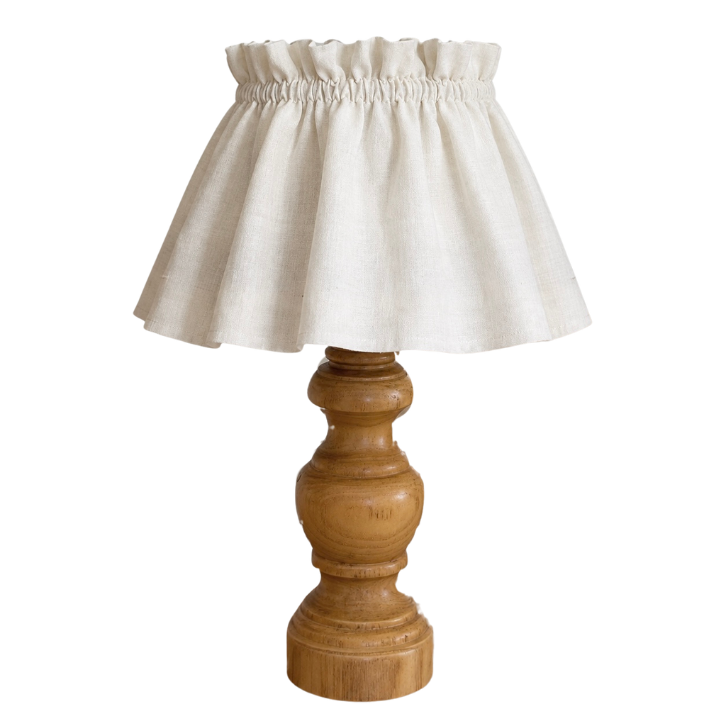 A table lamp with a natural beige linen ruffled shade and a turned wooden base, shown against a plain white background.