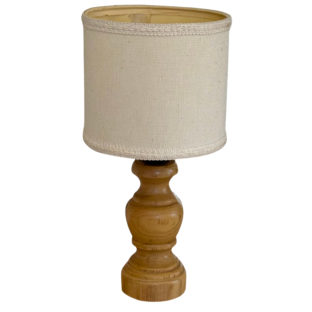A table lamp with a natural wood turned base and a beige linen drum shade, isolated on a white background.