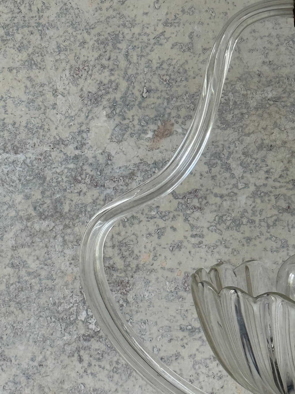 A close-up of a clear ribbed glass of murano pendant light on a mottled grey stone surface.