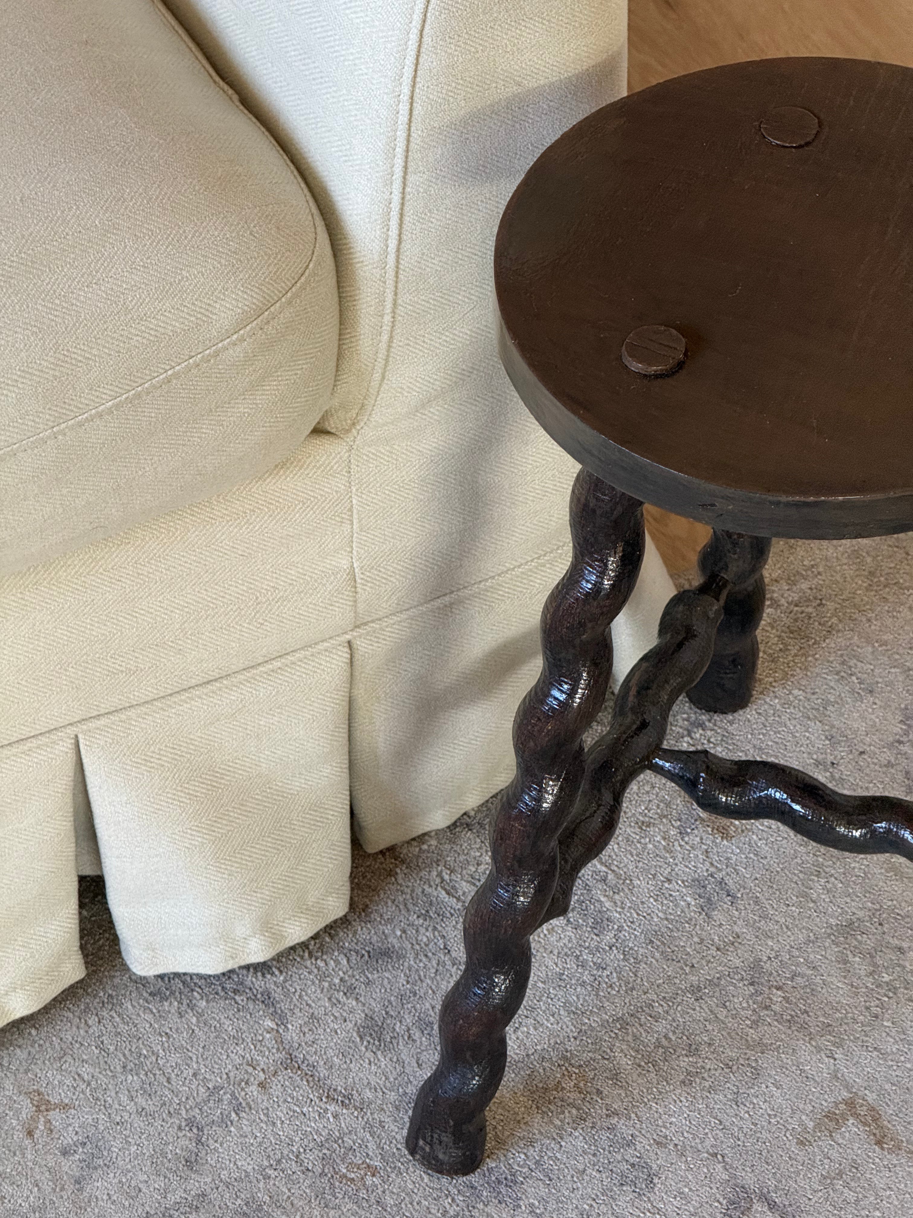 A close-up of a rustic dark wood side table with twisted, gnarled legs placed next to a cream-colored slipcovered sofa on a textured rug.