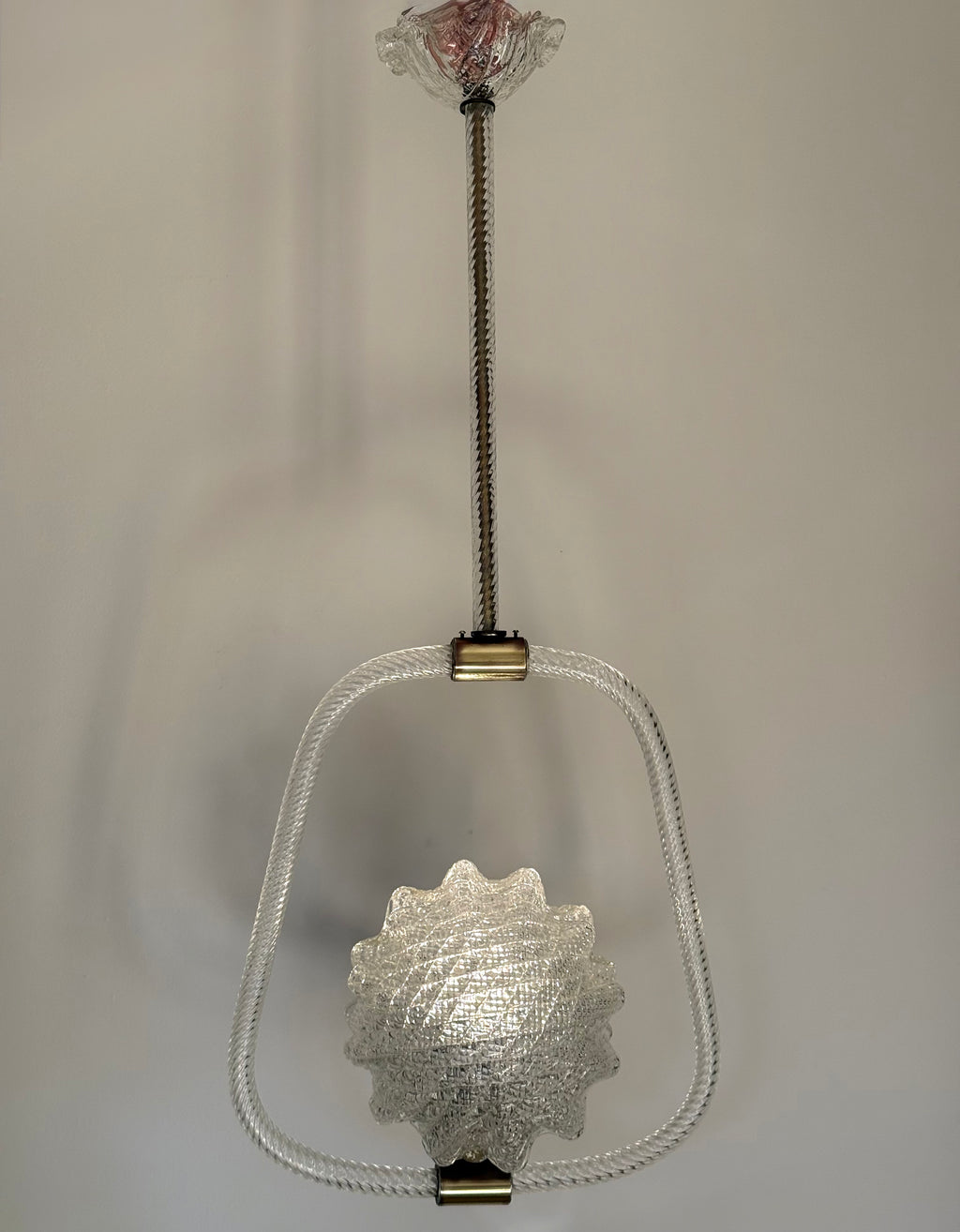 A vintage-style hanging light fixture with a textured clear glass shade, a clear glass oval frame, and brass-toned metal hardware against a plain light gray background.