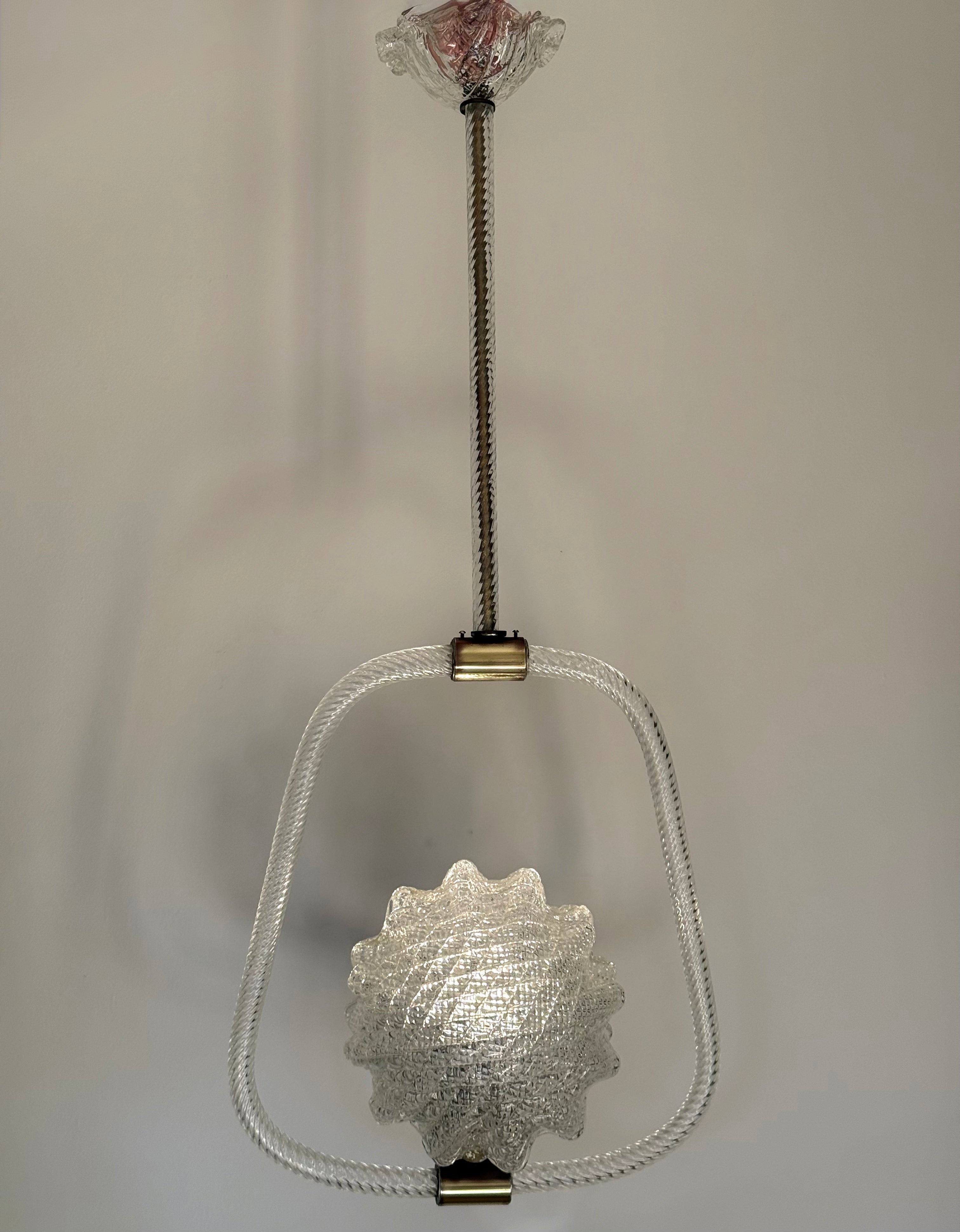 A vintage-style hanging light fixture with a textured clear glass shade, a clear glass oval frame, and brass-toned metal hardware against a plain light gray background.