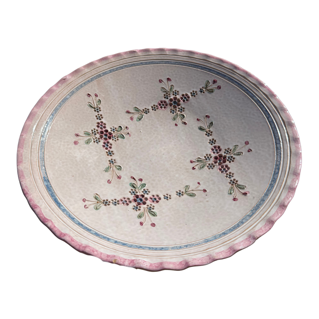An oval ceramic serving platter with a scalloped pink rim, featuring a central floral pattern with red, green, and blue details on a light beige background.