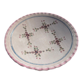 An oval ceramic serving platter with a scalloped pink rim, featuring a central floral pattern with red, green, and blue details on a light beige background.