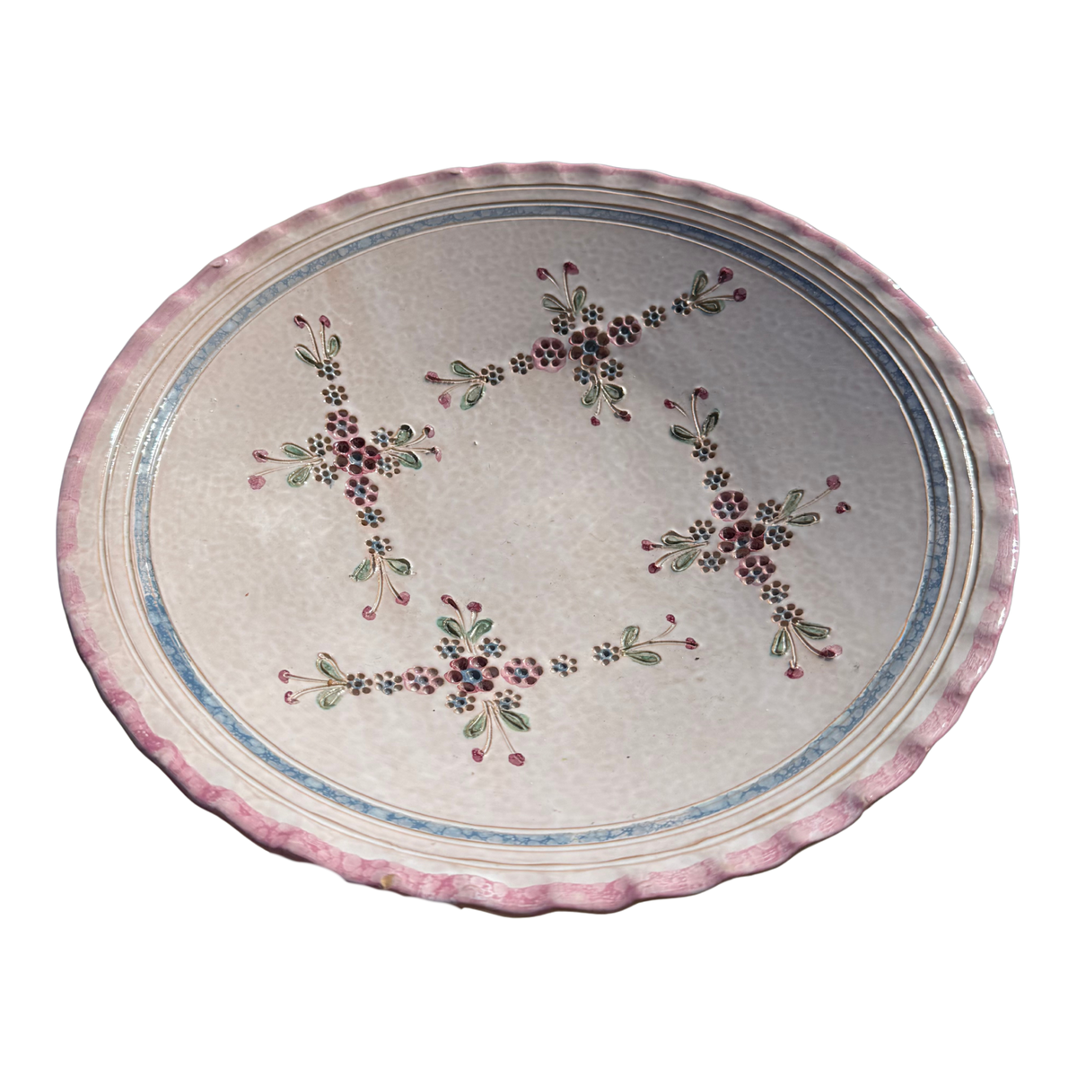 An oval ceramic serving platter with a scalloped pink rim, featuring a central floral pattern with red, green, and blue details on a light beige background.