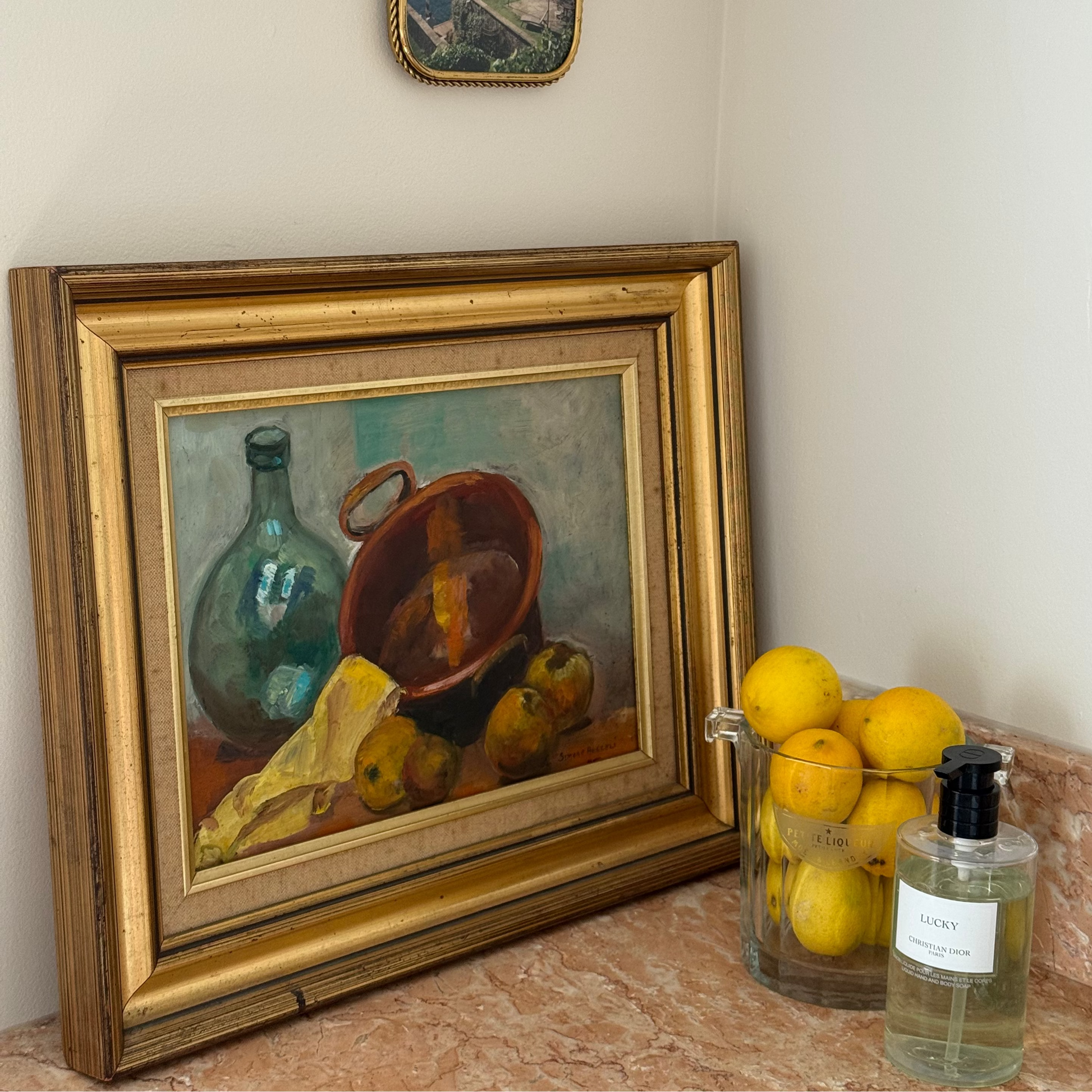 Framed still life painting on a marble surface with lemons and a bottle.